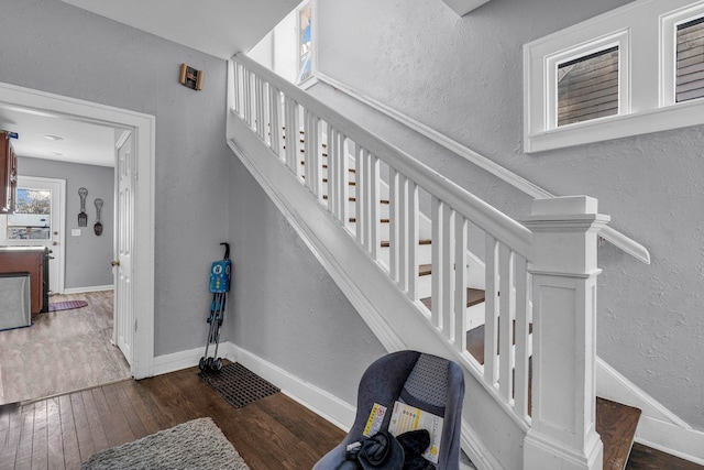 staircase featuring a textured wall, baseboards, and wood finished floors