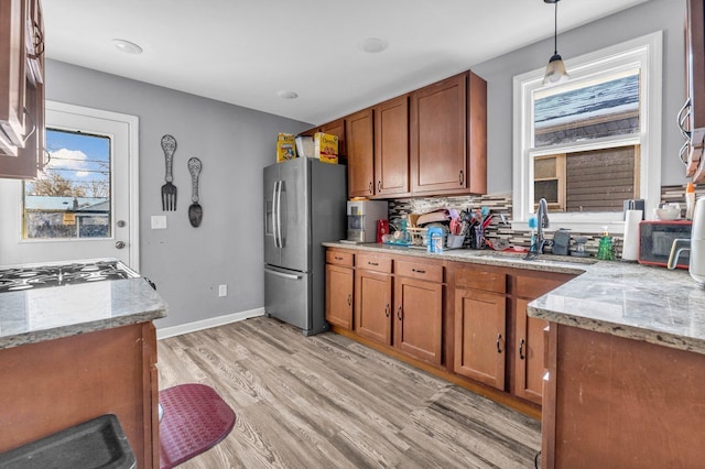 kitchen featuring stainless steel fridge, brown cabinets, hanging light fixtures, light stone countertops, and a sink