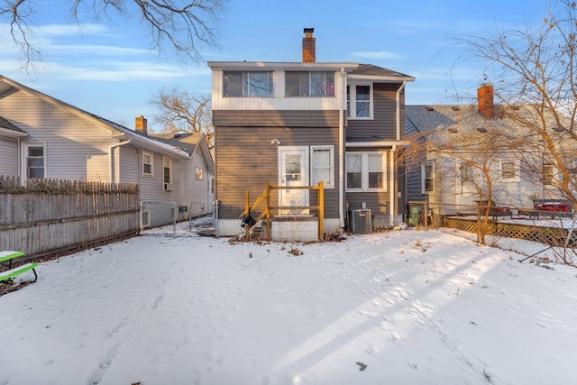 snow covered back of property with cooling unit, fence, and a chimney