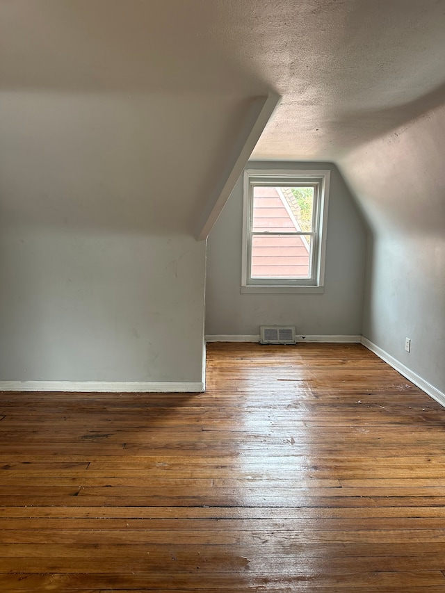 additional living space with a textured ceiling, lofted ceiling, dark wood-type flooring, visible vents, and baseboards