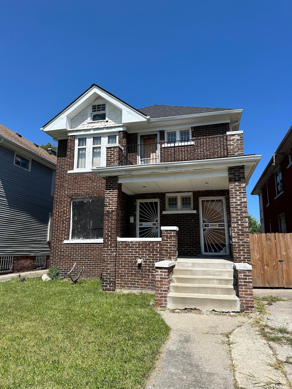 view of front facade featuring a balcony, fence, a front lawn, and brick siding