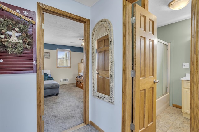 hall with light carpet, a textured ceiling, visible vents, and baseboards