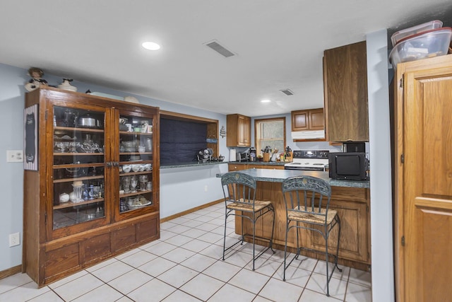 kitchen with light tile patterned floors, white range with electric stovetop, baseboards, visible vents, and under cabinet range hood