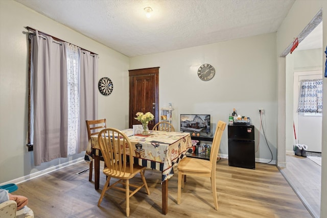 dining space featuring a textured ceiling, baseboards, and wood finished floors