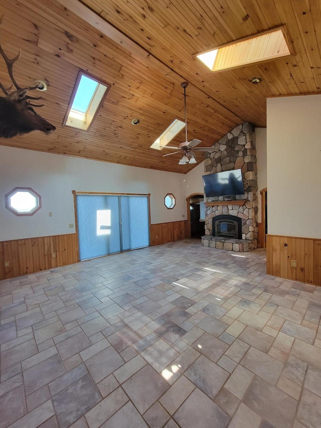 unfurnished living room featuring a skylight, a wainscoted wall, wood ceiling, a stone fireplace, and wood walls