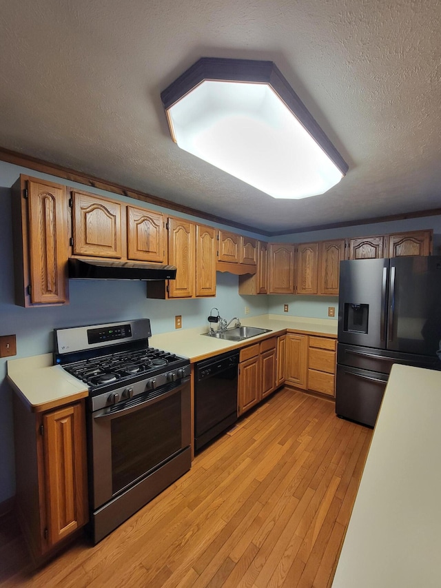 kitchen featuring under cabinet range hood, stainless steel appliances, a sink, light countertops, and light wood finished floors