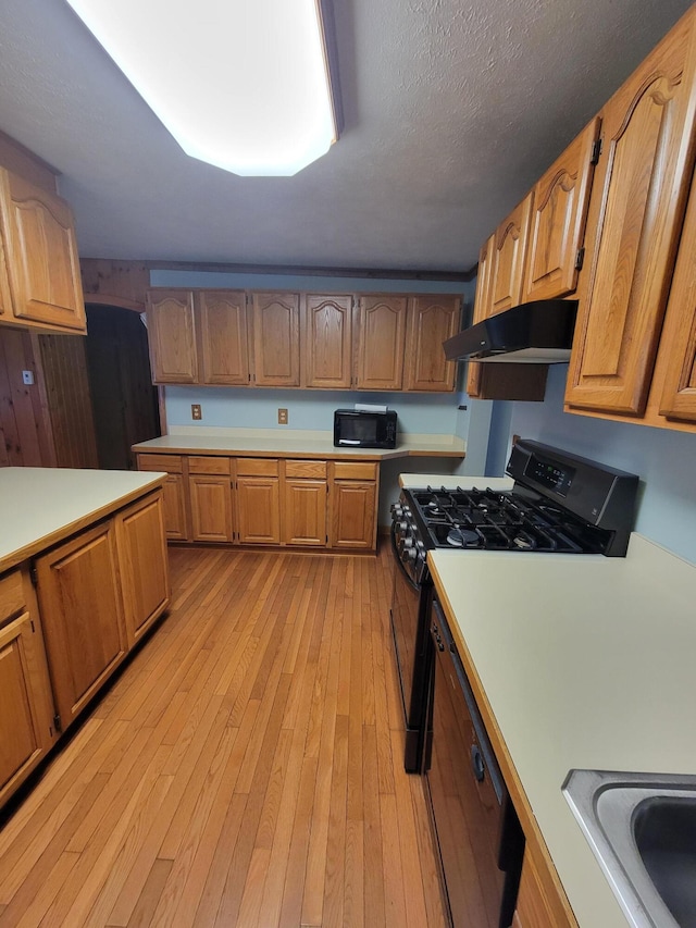 kitchen with a textured ceiling, under cabinet range hood, light wood-style floors, light countertops, and black appliances