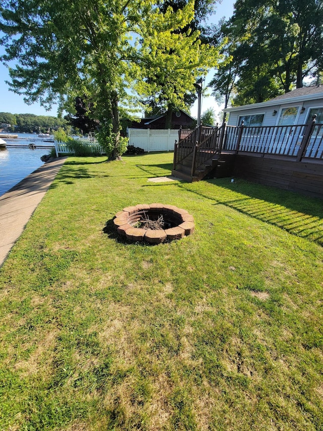 view of yard featuring an outdoor fire pit, a deck with water view, and fence