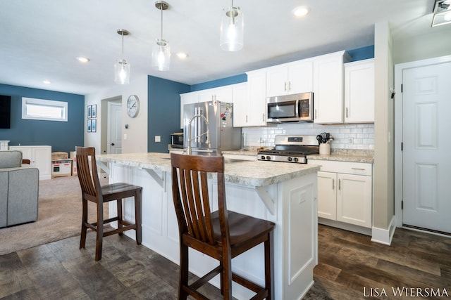 kitchen featuring stainless steel appliances, pendant lighting, light countertops, and an island with sink