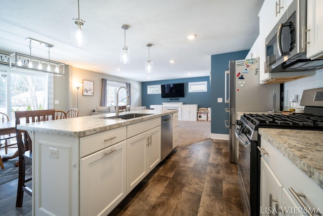 kitchen featuring decorative light fixtures, appliances with stainless steel finishes, a kitchen island with sink, white cabinetry, and a sink