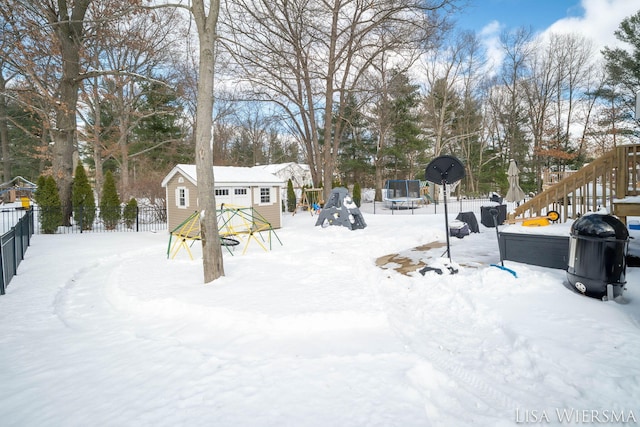 snowy yard with a storage shed, a trampoline, an outdoor structure, and fence