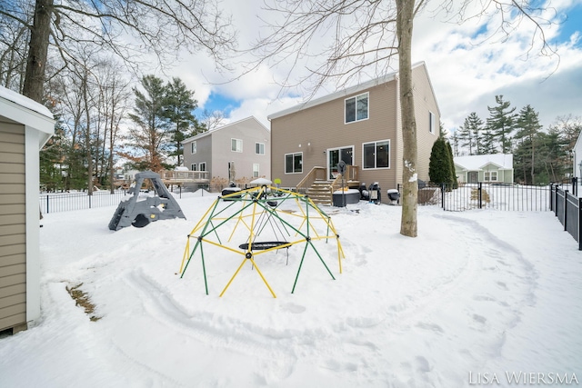 snow covered back of property featuring a playground and a fenced backyard