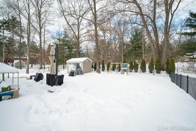 yard covered in snow with a storage shed, a playground, fence, and an outbuilding