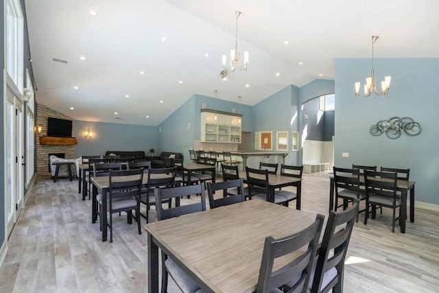 dining room featuring light wood-style floors, a fireplace, a notable chandelier, and high vaulted ceiling