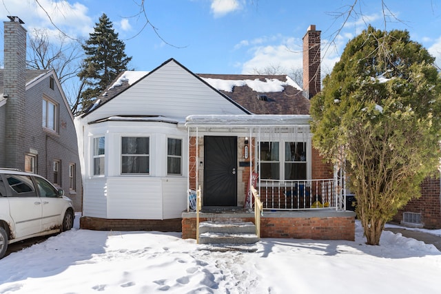 bungalow featuring a porch, brick siding, and a chimney