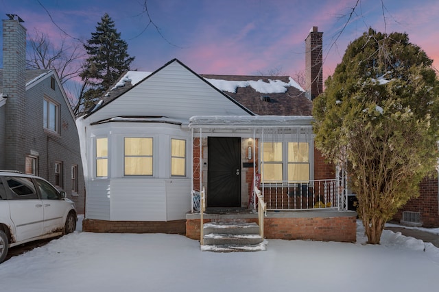 bungalow-style home featuring covered porch, brick siding, and a chimney