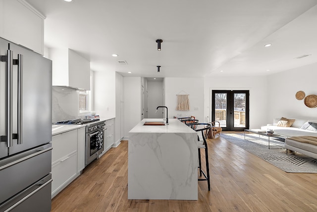 kitchen with french doors, light wood-style floors, a sink, wall chimney range hood, and high quality appliances