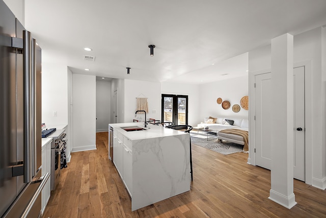 kitchen with a center island with sink, visible vents, light wood-style floors, a sink, and high quality appliances