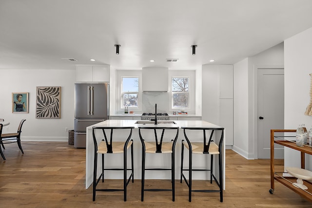 kitchen with a kitchen island with sink, high quality fridge, white cabinetry, and light wood-style floors