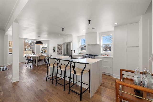 kitchen with high end fridge, light wood-style flooring, white cabinets, a kitchen island with sink, and a sink