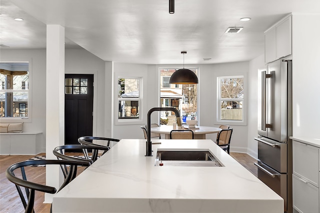 kitchen featuring light wood-style flooring, a sink, visible vents, high end fridge, and a center island with sink