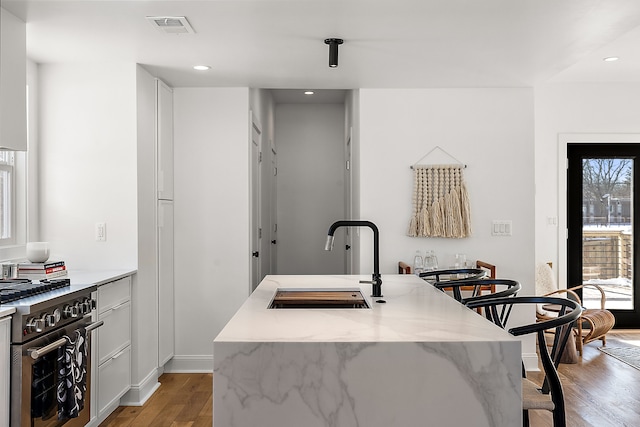 kitchen featuring high end stove, a sink, visible vents, a kitchen breakfast bar, and light wood-style floors