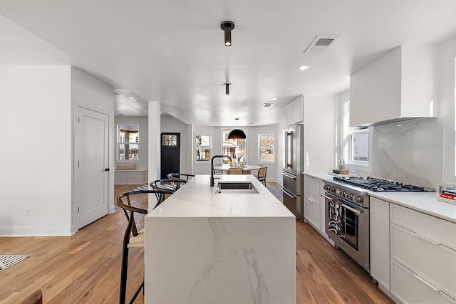 kitchen with a breakfast bar, visible vents, a sink, wall chimney range hood, and high quality appliances