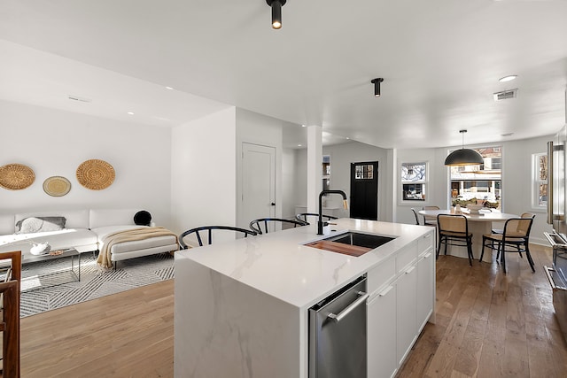 kitchen with a sink, visible vents, light countertops, stainless steel dishwasher, and wood-type flooring