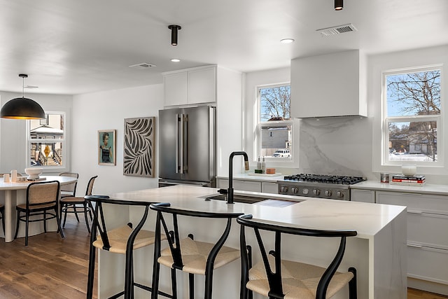 kitchen featuring stainless steel appliances, dark wood-style flooring, a sink, visible vents, and wall chimney range hood