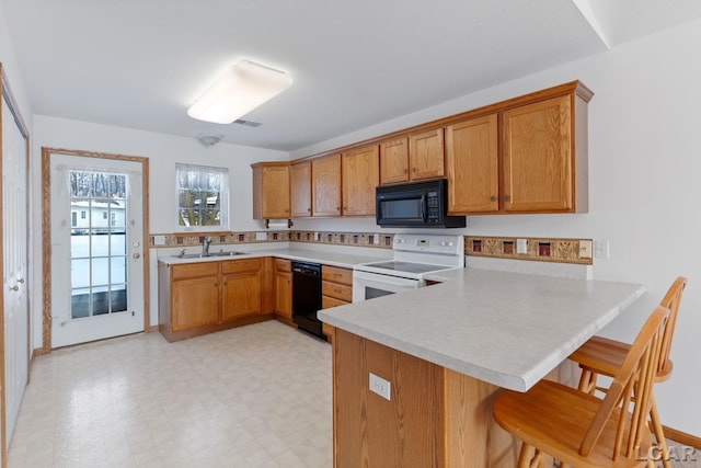 kitchen featuring a breakfast bar area, light floors, a peninsula, light countertops, and black appliances