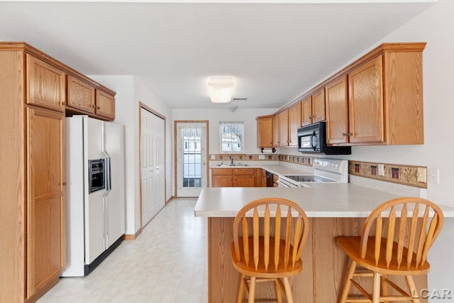 kitchen featuring white appliances, light countertops, a peninsula, and a kitchen breakfast bar