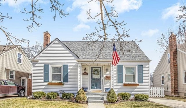 view of front of house featuring a chimney, fence, a front lawn, and roof with shingles