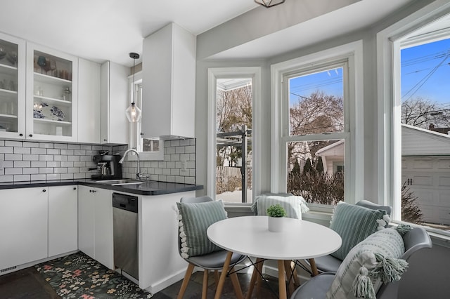 kitchen featuring a sink, white cabinets, stainless steel dishwasher, backsplash, and dark countertops