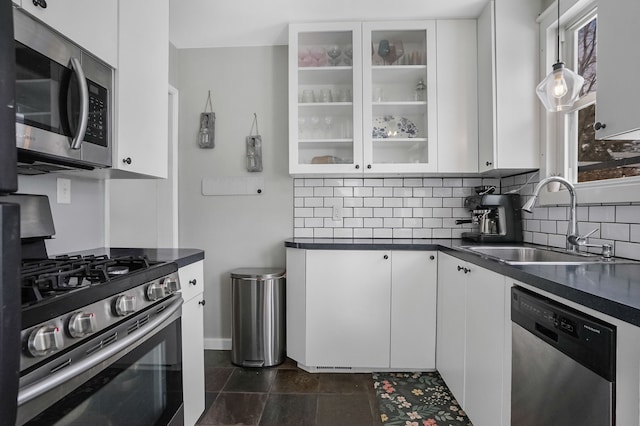 kitchen with dark countertops, a sink, stainless steel appliances, white cabinetry, and backsplash