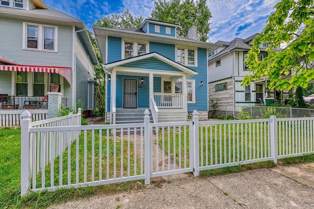 american foursquare style home featuring covered porch, a fenced front yard, and a front yard