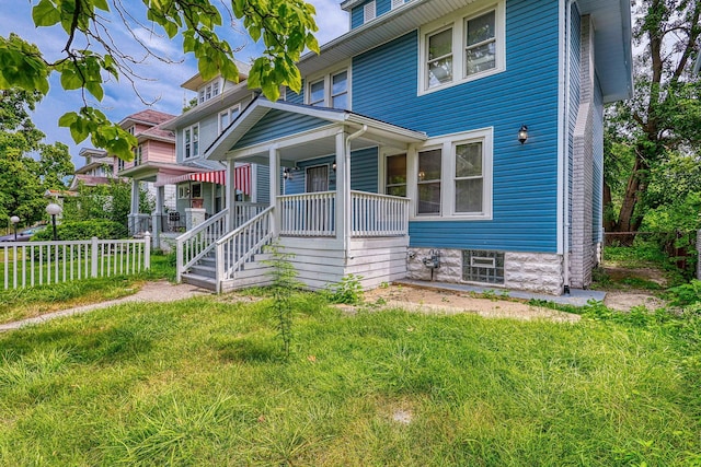 american foursquare style home featuring a porch, a front lawn, and fence