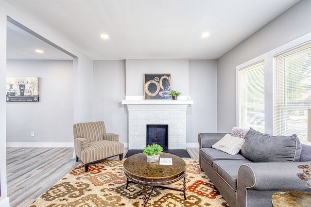 living area featuring light wood finished floors, a brick fireplace, baseboards, and recessed lighting