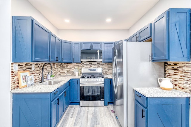 kitchen featuring a sink, blue cabinetry, appliances with stainless steel finishes, backsplash, and light wood finished floors