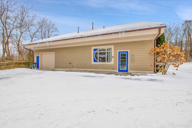 snow covered back of property featuring fence and a detached garage