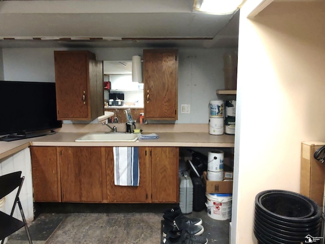 kitchen featuring brown cabinetry, light countertops, a sink, and concrete flooring