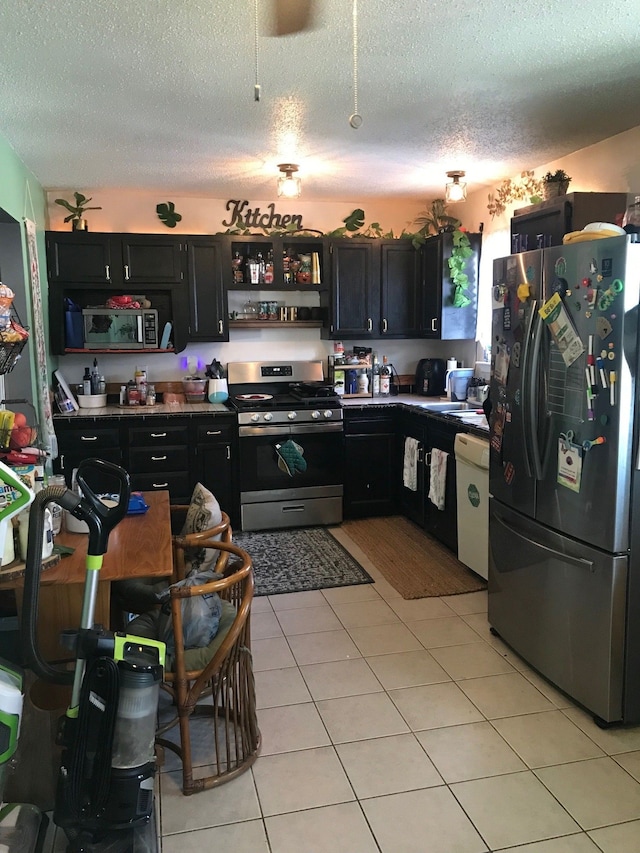 kitchen with a textured ceiling, appliances with stainless steel finishes, dark cabinets, and light tile patterned flooring