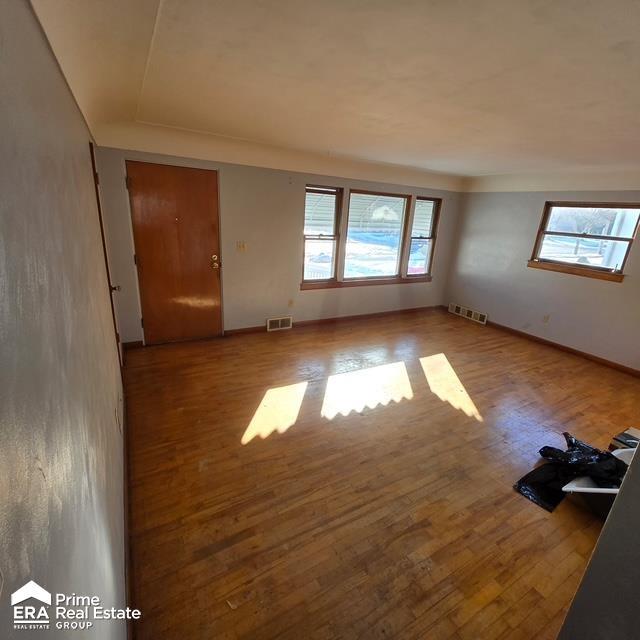 unfurnished room with a wealth of natural light, visible vents, and hardwood / wood-style flooring