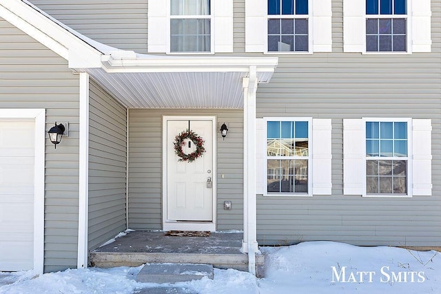 snow covered property entrance featuring a garage