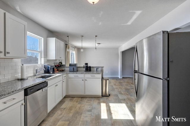 kitchen featuring a peninsula, light stone countertops, white cabinetry, and appliances with stainless steel finishes