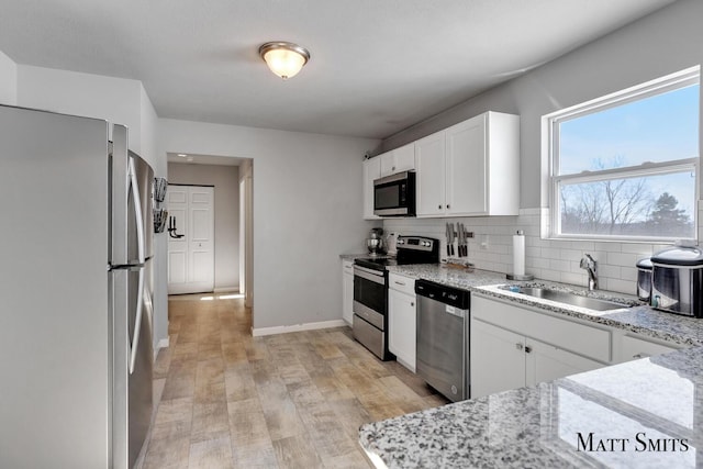 kitchen featuring tasteful backsplash, appliances with stainless steel finishes, light stone counters, white cabinetry, and a sink