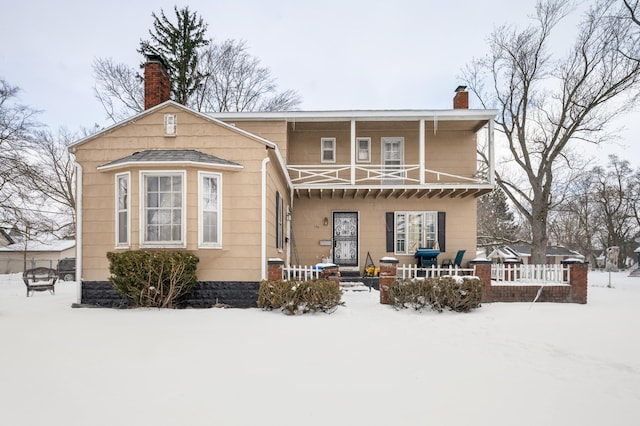 snow covered property with a balcony, a chimney, and fence