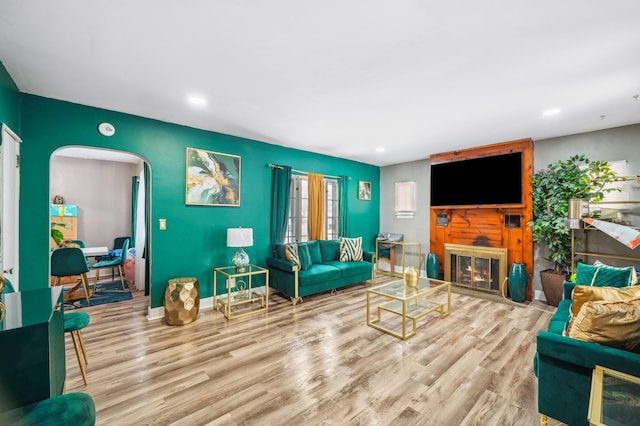 living area featuring arched walkways, recessed lighting, a large fireplace, baseboards, and light wood finished floors