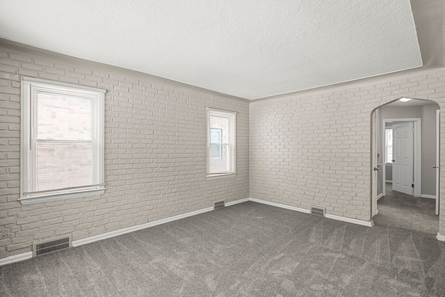 spare room with arched walkways, visible vents, dark carpet, and a textured ceiling