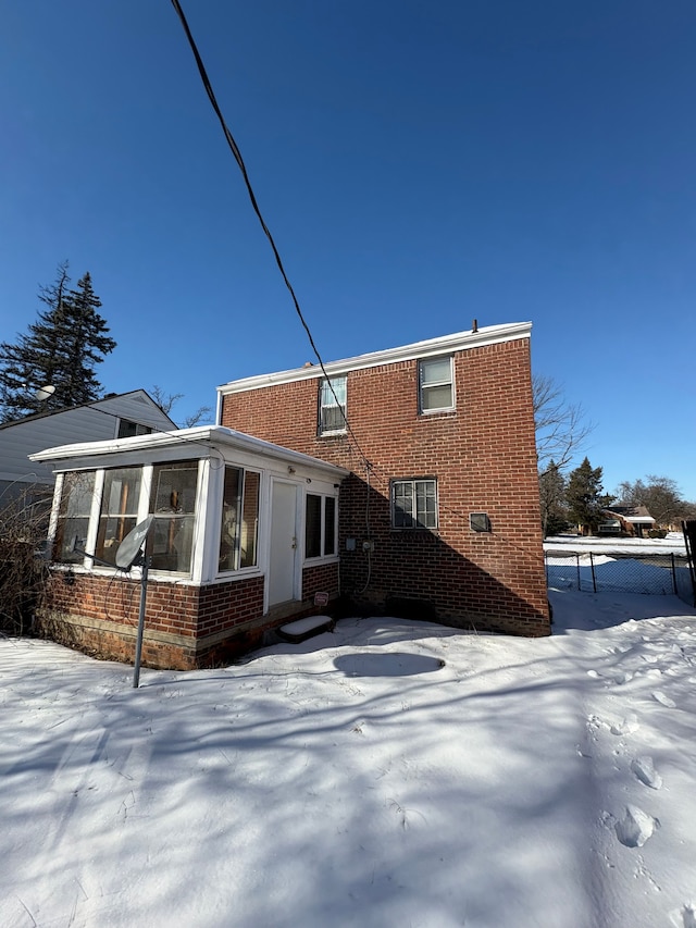 snow covered back of property with brick siding and a sunroom