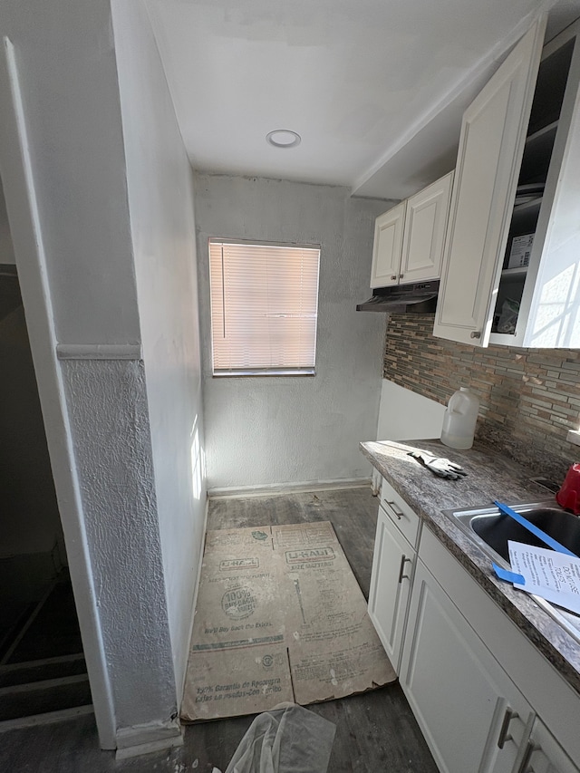 kitchen with a textured wall, dark wood-type flooring, a sink, white cabinetry, and tasteful backsplash